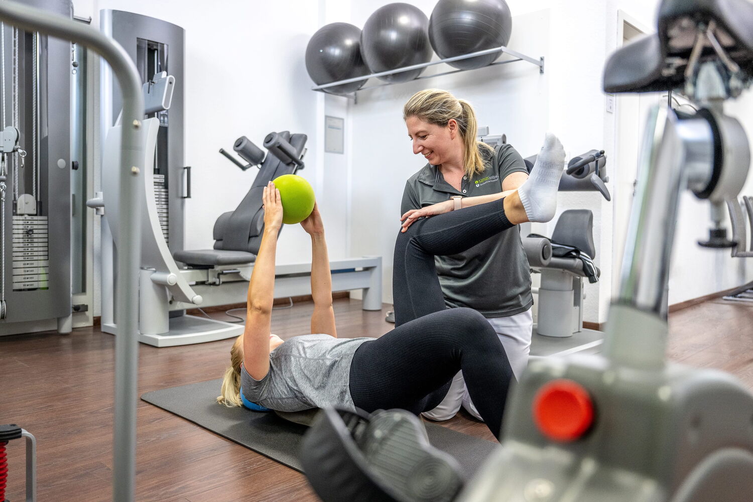 Eine Frau erhält persönliches physiktherapeutisches Training, Sie hält einen Trainingsball nach oben und hat das Knie angewinkelt.