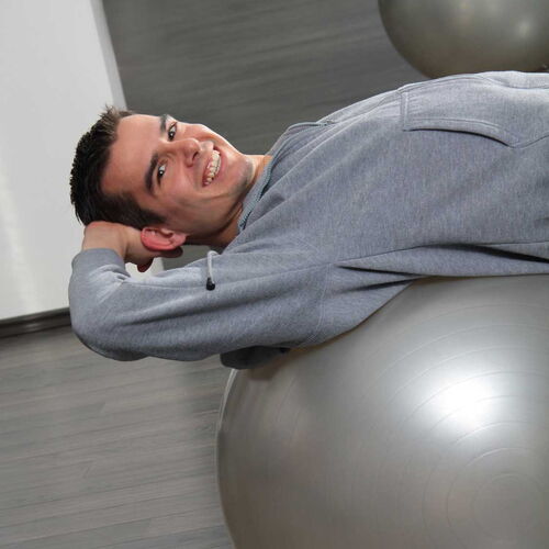 Mann liegt auf einem solbernen Ball und macht Krankengymnastik.