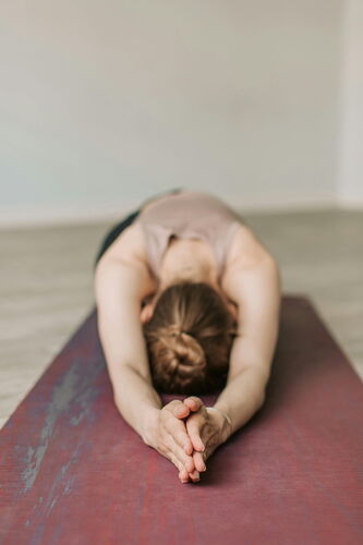 Eine Frau vollzieht Yoga Übungen auf einer Yogamatte. Sie ist nach Vorne gebeugt und hält die Arme nach vorne.