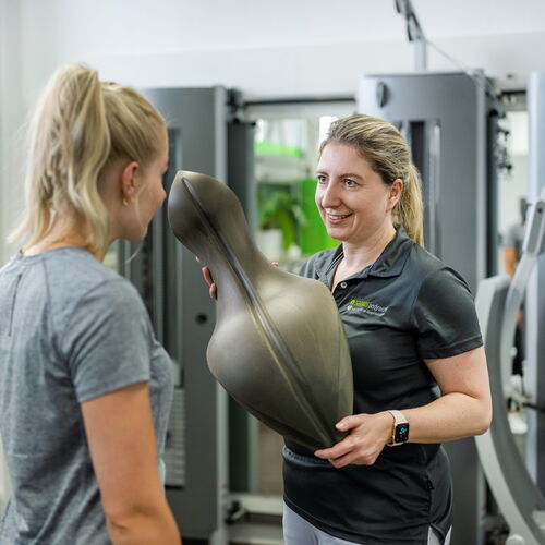 Eine Trainerin weist eine Patientin in das Training ein.